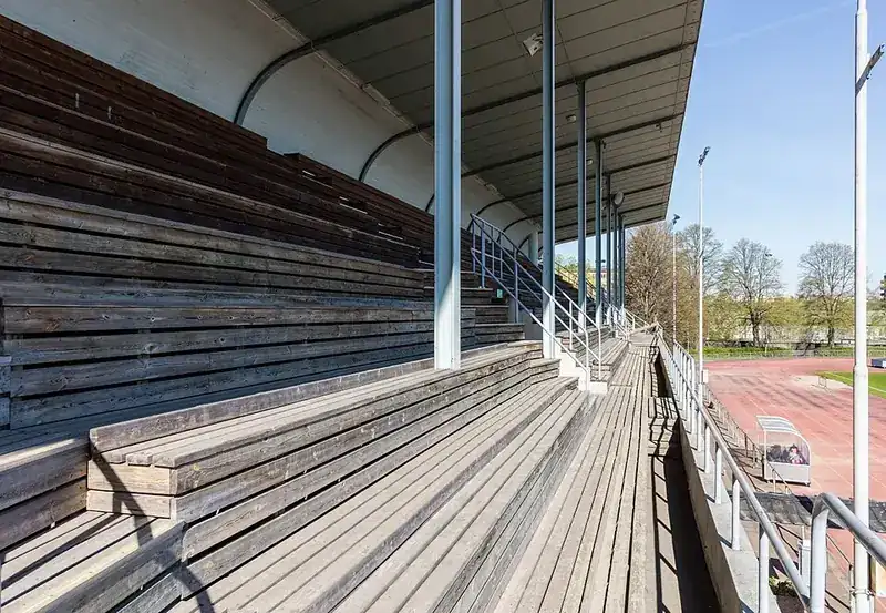 Träläktare med bänkrader under tak vid en idrottsplats, tom före match